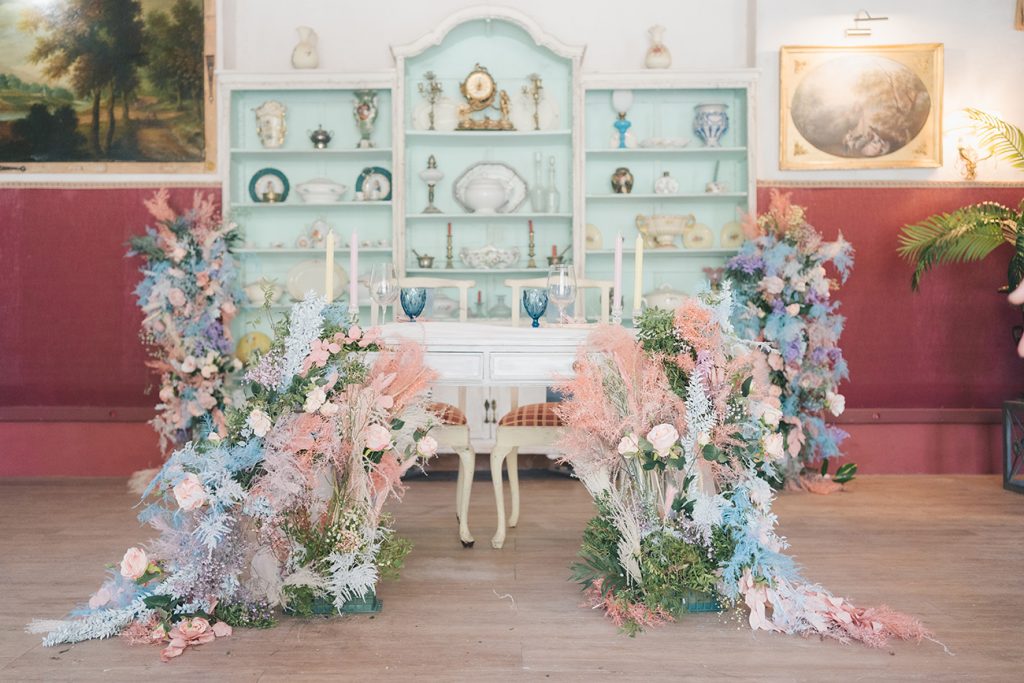Decoración de mesa presidencial con flores de colores pastel frente a una antigua y bonita alacena