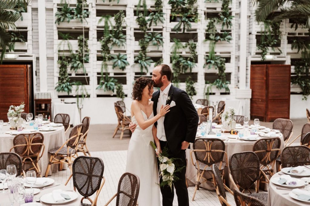 Novios de pie en el salón del banquete de su boda dándose un beso